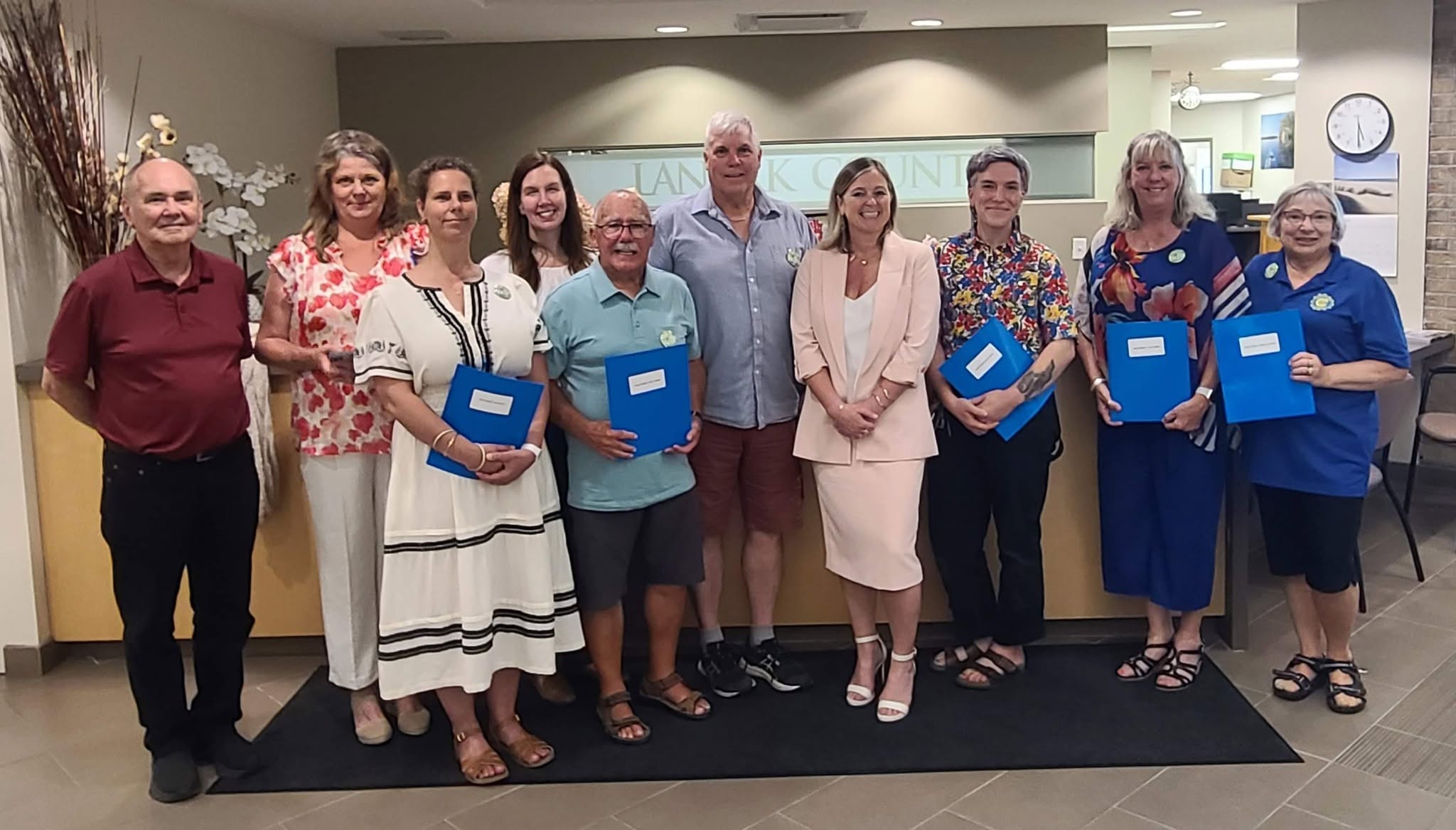 A group of people stand together for a photo holding blue folders
