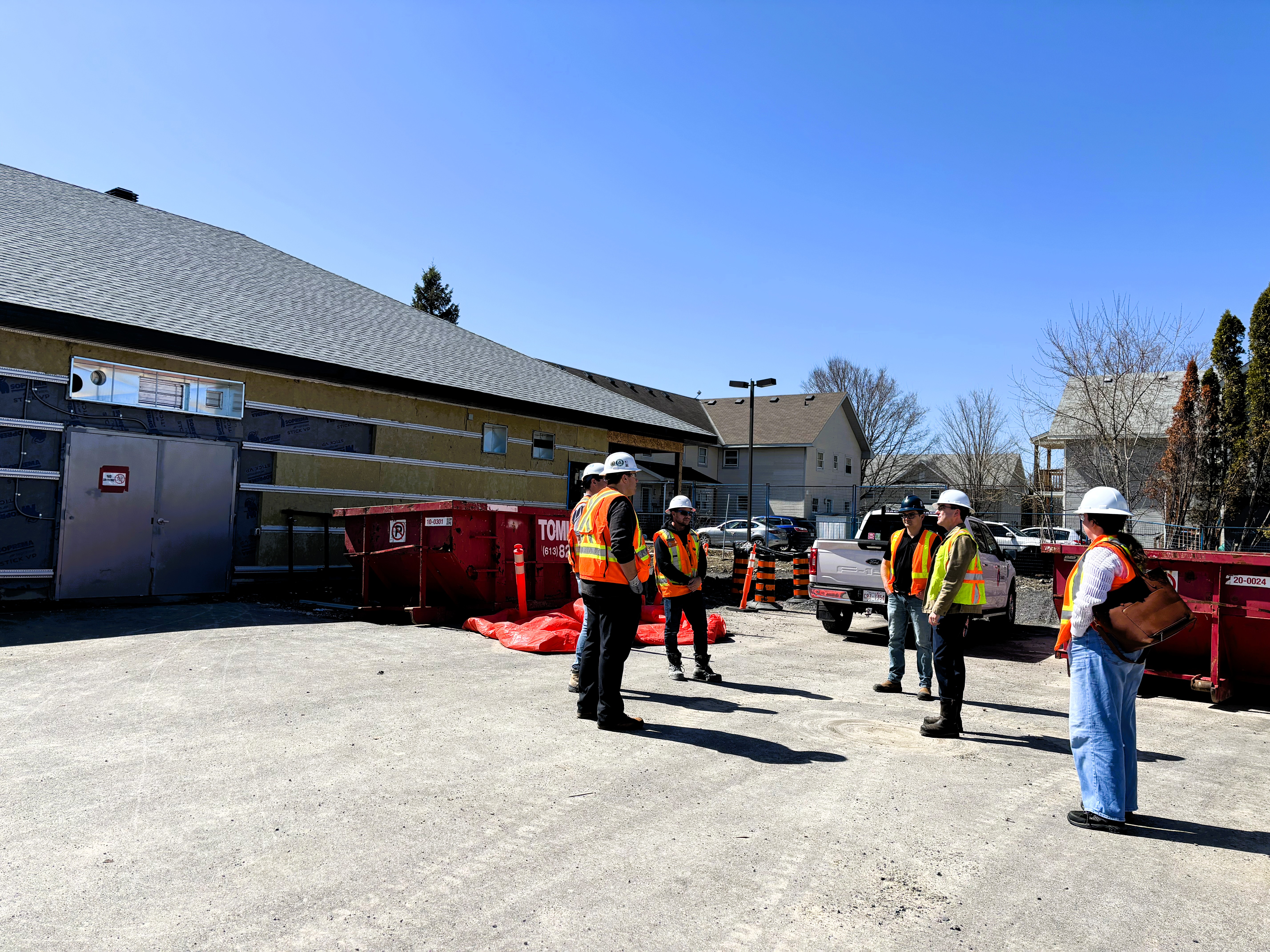 People wearing hard hats and orange and yellow construction vests stand outside a building under construction