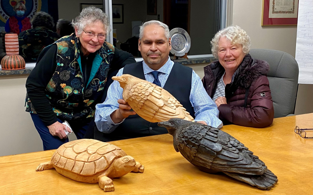 Three people seated at a table surrounded by wooden carvings of animals