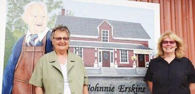 Two women stand in front of a painted mural outside