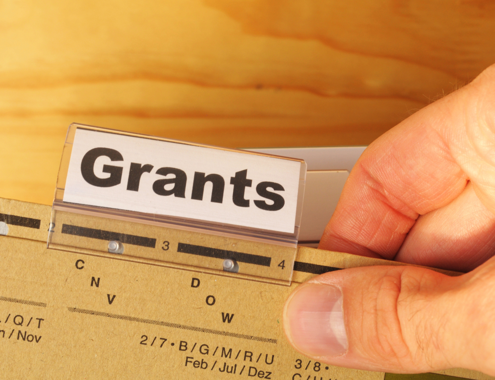 Hand pulls file out of folder marked 'Grants'