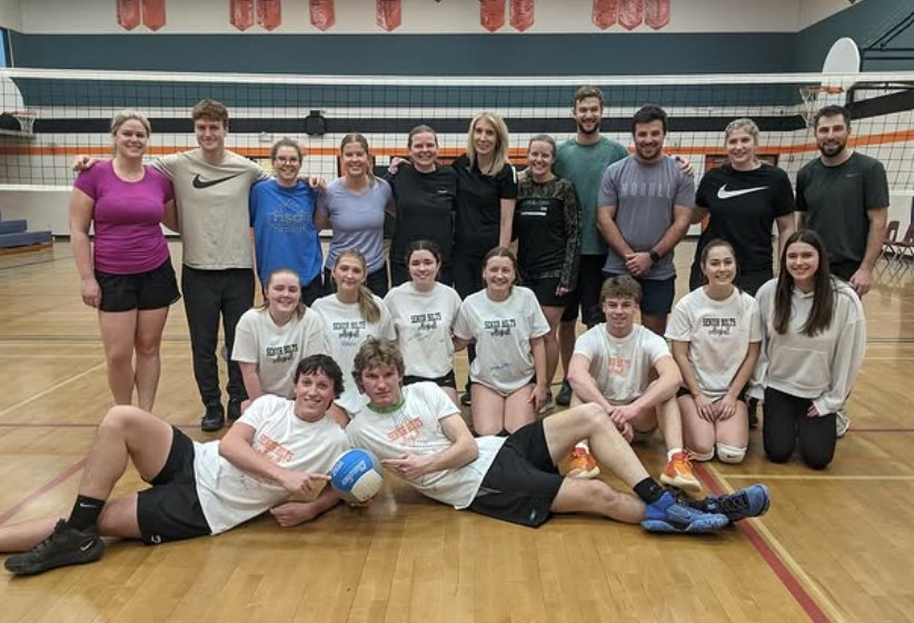 A group of people stand for a photo in a school gymnasium