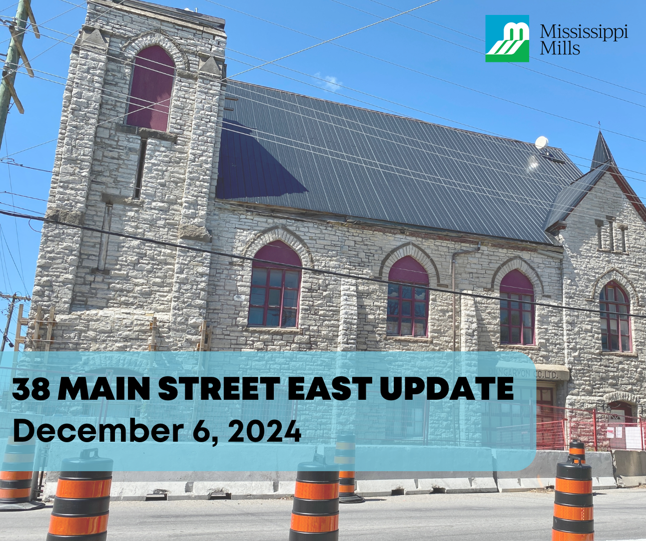 A stone building surrounded by concrete barriers and orange pylons with the text '38 Main Street East Update - December 6, 2024'